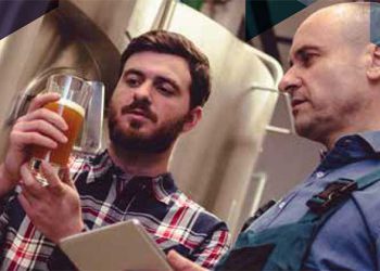 people talking looking at a beer in a manufacturing facility